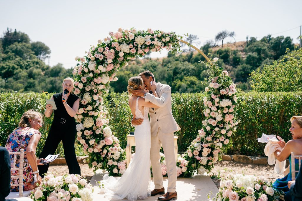 Vici and Martin kissing under the flower arch, Casa de la Era wedding in Marbella