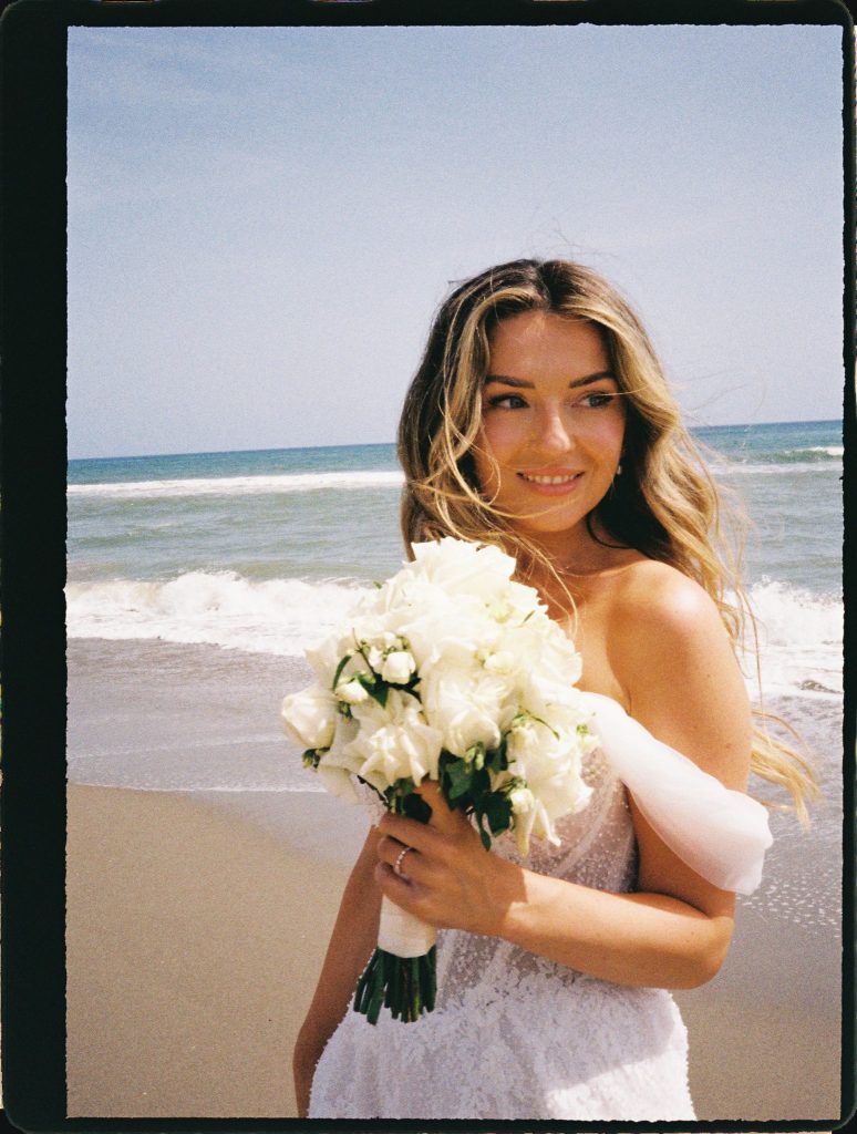 Bride with a white bouquet smiling by the sea, 35mm film wedding photo on the Costa del Sol