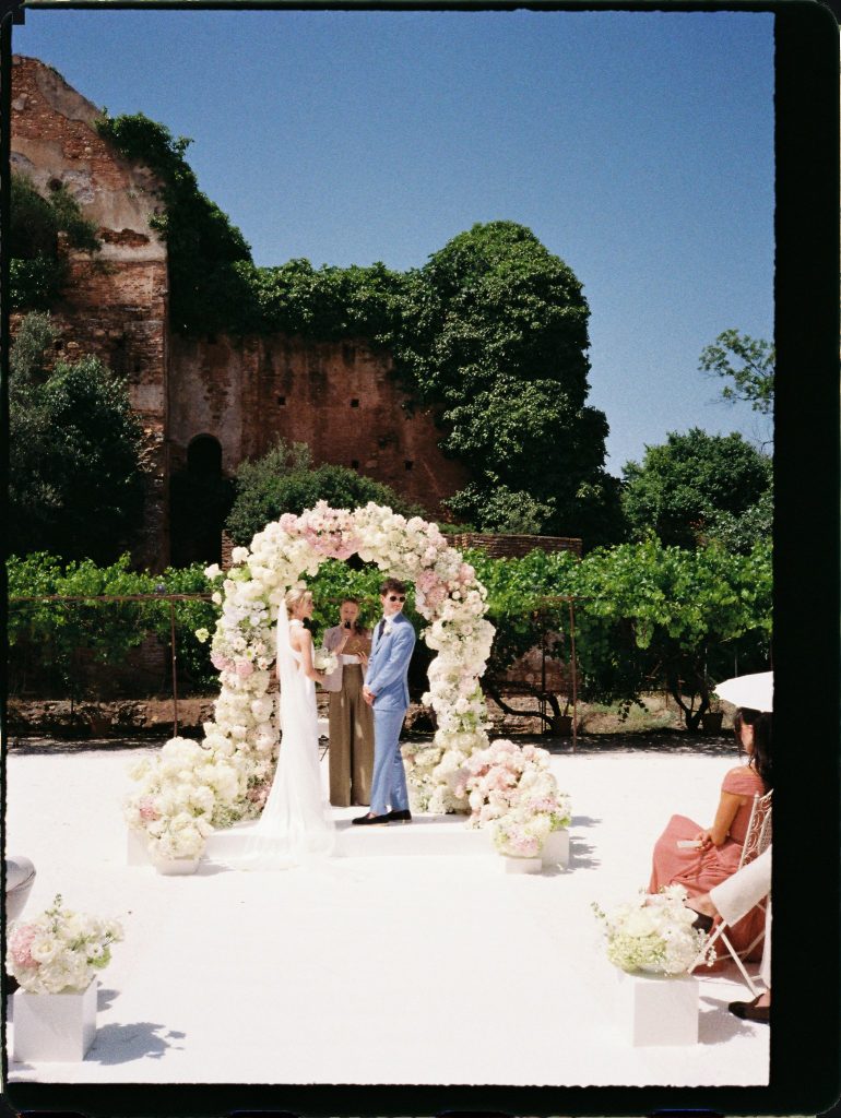 Wedding ceremony under a flower arch beside old stone walls, 35mm film wedding photo on the Costa del Sol