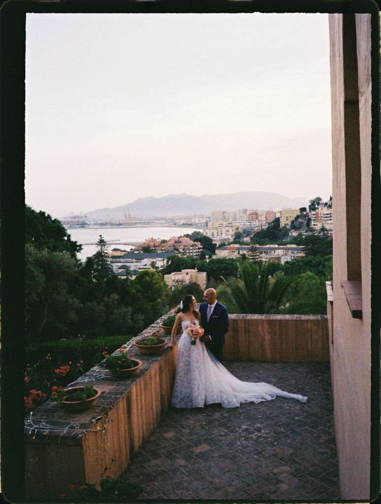 Bride and groom on a terrace with the sea and the city behind them, 35mm film wedding photo on the Costa del Sol